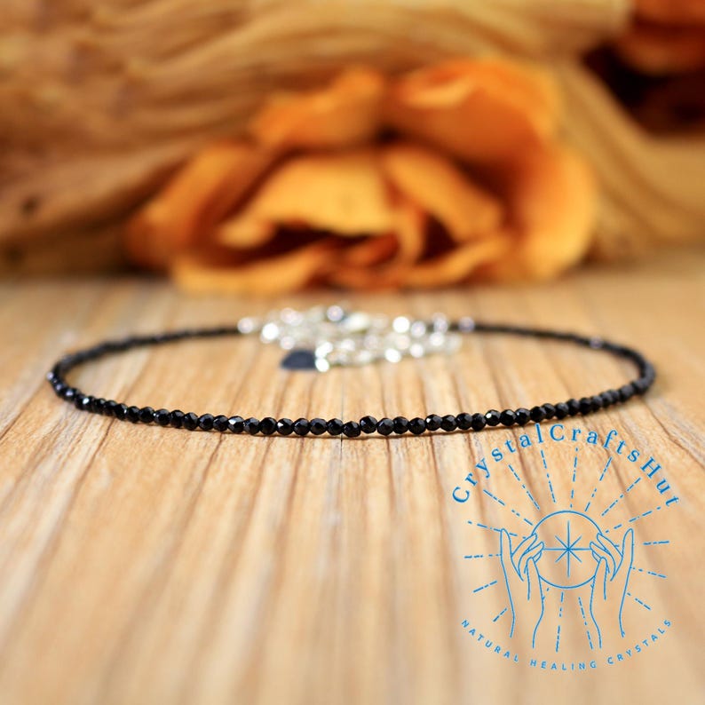 Pu&ograve; includere: Una delicata collana nera a choker realizzata con piccole perle di onice nero. La collana &egrave; su una superficie di legno.