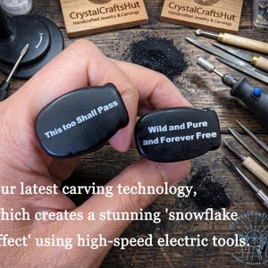 May include: Two black, oval-shaped carvings with white text reading "This too Shall Pass" and "Wild and Pure and Forever Free." The carvings are held near carving tools and a rotary tool. The image shows the CrystalCraftsHut logo.
