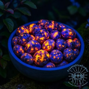 May include: A blue bowl filled with glowing, spherical stones. The stones have a dark blue base color with vibrant orange and yellow patterns. The bowl is set against a dark green, leafy background. The image has a mystical, natural theme.
