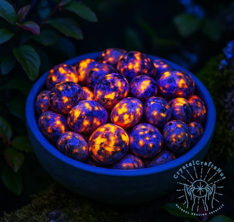 May include: A blue bowl filled with glowing, spherical stones. The stones have a dark blue base color with vibrant orange and yellow patterns. The bowl is set against a dark green, leafy background. The image has a mystical, natural theme.