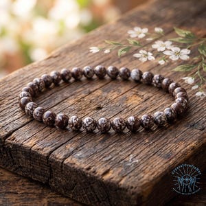 May include: A circular bracelet composed of small, round, dark brown beads featuring a distinct white snowflake-like pattern throughout. The beads are strung together in a continuous loop, displaying a smooth, polished finish on each individual stone.