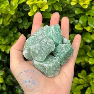 May include: A handful of rough, green aventurine crystals. The crystals are a light, opaque green with a slightly textured surface. The image includes the text "Crystal Crafts Hut" in a circular design.