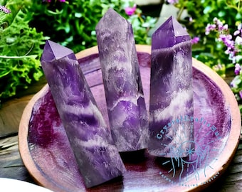 May include: Three purple amethyst crystal points with white swirls, arranged on a purple plate. The plate has the text "Crystal Crafts by Emma" and "Natural Healing Crystals" on it.