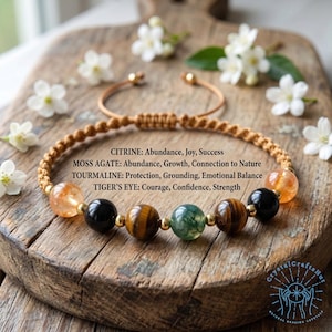Puede incluir: Una pulsera de cuentas con un cordón de macramé, con piedras de citrino, ágata musgosa, turmalina y ojo de tigre. La pulsera se muestra sobre una superficie de madera con flores blancas.