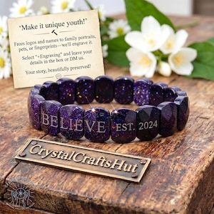 May include: A dark purple bracelet with the word "BELIEVE" engraved on it, along with "EST. 2024". The bracelet is made of faceted, rectangular beads with a glittery effect. The image also includes text that says "Make it unique youth!" and "Crystal Crafts Hut".