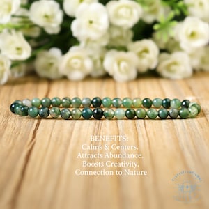 May include: A green beaded bracelet with a mix of dark and light green beads. The bracelet is displayed on a wooden surface with white flowers in the background. Text on the image reads "BENEFITS: Calms & Centers. Attracts Abundance. Boosts Creativity. Connection to Nature."