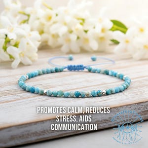 May include: A blue beaded bracelet with silver accents. The bracelet is on a wooden surface with white flowers in the background. Text on the image reads: "Promotes Calm, Reduces Stress, Aids Communication."