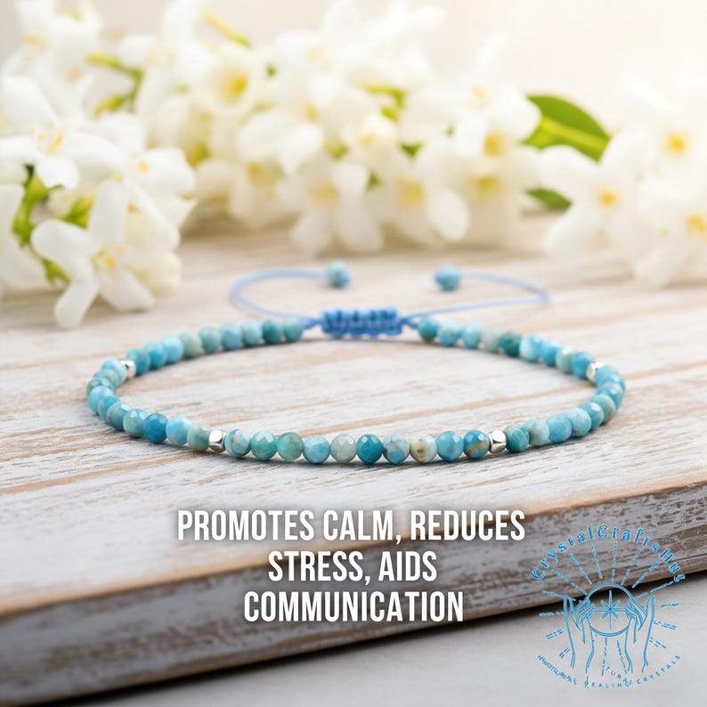 May include: A blue beaded bracelet with silver accents. The bracelet is on a wooden surface with white flowers in the background. Text on the image reads: "Promotes Calm, Reduces Stress, Aids Communication."
