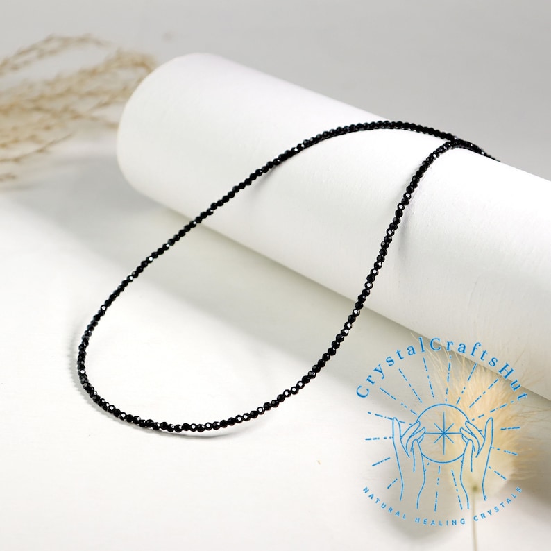 K&ouml;nnte beinhalten: Eine schwarze Perlenkette aus kleinen, facettierten schwarzen Onyxperlen. Die Kette liegt auf einer wei&szlig;en Oberfl&auml;che.