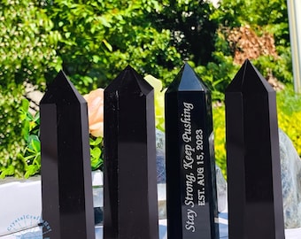 May include: Four black obsidian obelisks with pointed tops. One obelisk has the text "Stay Strong, Keep Pushing" and "EST. AUG 15, 2023" etched on it. The obelisks are displayed in front of a green and white background.