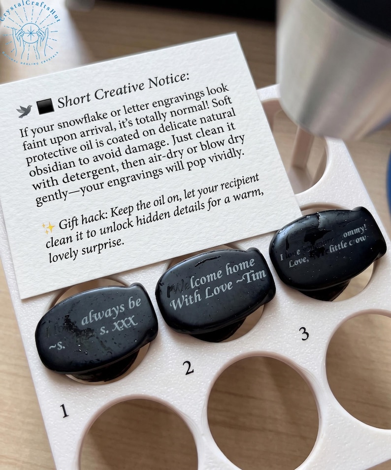 May include: Three black obsidian stones with engraved messages, including "always be s. XXX", "Welcome home With Love ~Tim", and "I love ommy! little crow". The stones are in a light pink holder with a card that has text.