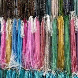 Pu&ograve; includere: Una variet&agrave; di fili di perline colorate appese a un muro. I fili sono fatti di diversi materiali, tra cui vetro, metallo e legno. Le perline sono di varie forme e dimensioni, e i colori sono vivaci e vibranti.