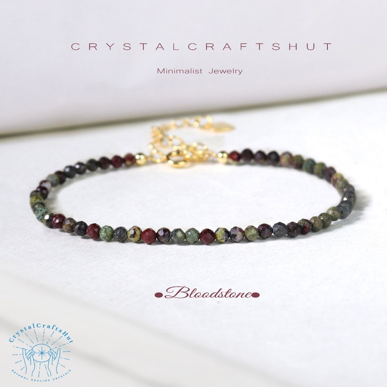 May include: A minimalist bloodstone bracelet with small, faceted beads in shades of green, red, and gray. The bracelet has a gold-colored chain and clasp. The text "CRYSTALCRAFTSHUT" and "Minimalist Jewelry" are at the top.