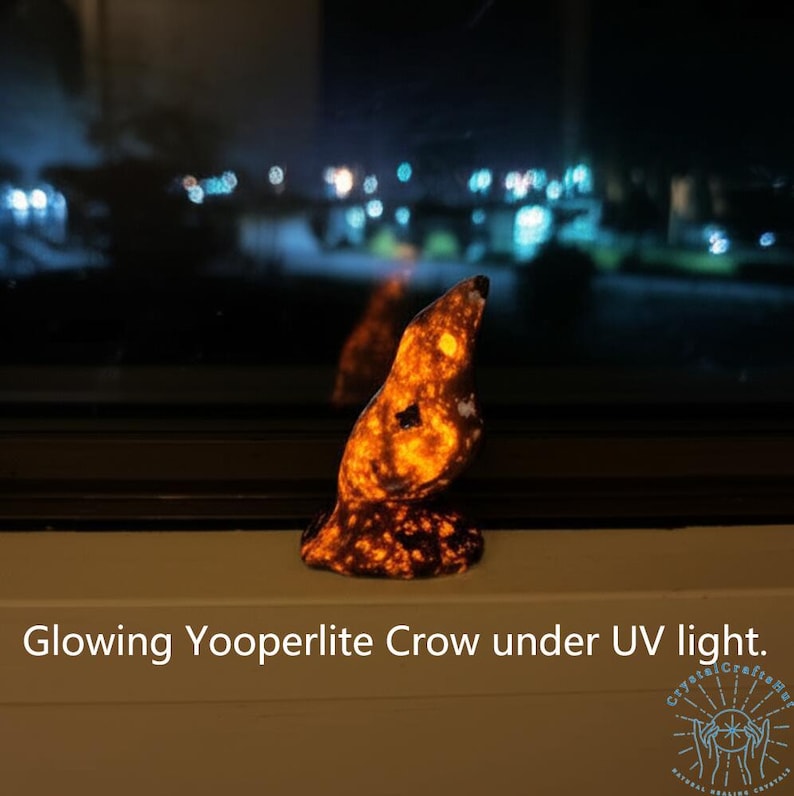 May include: A glowing Yooperlite crow figurine under UV light. The crow is orange and black, with a textured surface. The text "Glowing Yooperlite Crow under UV light" is at the bottom of the image.