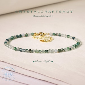 May include: A minimalist bracelet made of moss agate beads, with a gold-coloured clasp. The beads are small and round, in shades of green and white. The text "CRYSTALCRAFTSHUY Minimalist Jewelry" and "Moss Agate" are visible.