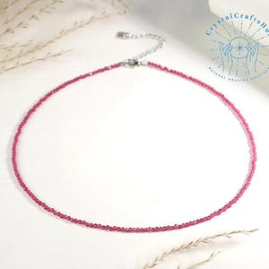 Könnte beinhalten: Eine zarte, magentafarbene Perlenkette mit einem silberfarbenen Verschluss. Die Kette wird auf weißem Untergrund präsentiert, mit dem Text "Crystal Crafts Hut" und einem Logo rechts oben. Die Kette ist etwa 35.5 cm lang.