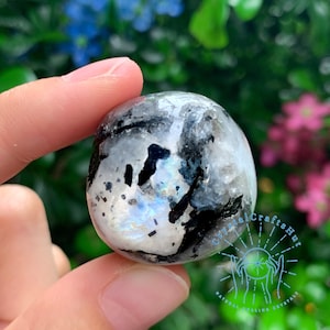 May include: A smooth, round, white and black gemstone with iridescent rainbow colors. The stone is being held in a hand.