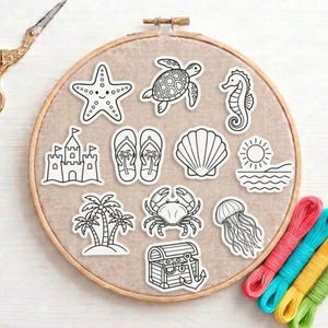 May include: A collection of black and white beach-themed stickers, including a starfish, turtle, seahorse, sandcastle, flip-flops, seashell, sun over water, palm trees, crab, jellyfish, and treasure chest. The stickers are arranged on a beige fabric within an embroidery hoop.