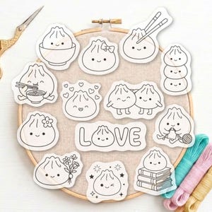 Può includere: Una collezione di dodici adesivi bianchi fustellati con disegni a linee nere di graziosi ravioli sorridenti in varie attività, tra cui tenere bacchette, lavorare a maglia e leggere libri, disposti su un telaio da ricamo in legno.