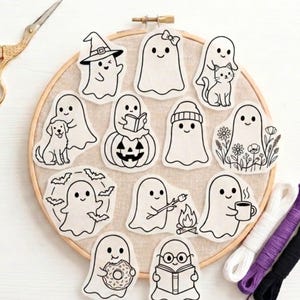 May include: A collection of twelve white fabric patches featuring black line art illustrations of ghosts in various activities, including reading, holding a cat, sitting on a pumpkin, roasting a marshmallow, and drinking coffee, arranged on a wooden hoop.