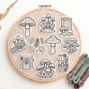May include: A selection of mushroom-themed stickers in various shapes and sizes, presented on an embroidery hoop. The stickers are outlined in black and feature detailed illustrations of different mushroom varieties, leaves, and a well. Embroidery floss and scissors are also visible.