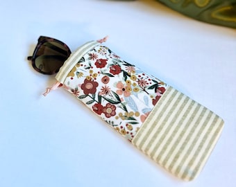 May include: A floral patterned eyeglasses case with a striped fabric bottom. The case is made of a soft, cream-colored fabric with a floral pattern in shades of red, pink, and yellow. The bottom of the case is made of a striped fabric in shades of beige and cream.