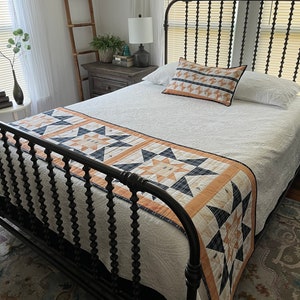 May include: A white bed with a black metal headboard and footboard. The bed has a white quilt and a patterned throw pillow. There is a black and white patterned bed runner on the bed.