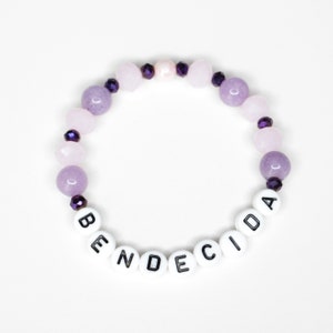 May include: A purple and white beaded bracelet with the word "BENDECIDA" spelled out in white beads.