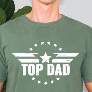 May include: A green t-shirt with a white graphic of a star and wings with the text "TOP DAD" in a circle of stars.