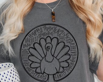 Puede incluir: Una camiseta gris con un gráfico negro de un pavo rodeado de las palabras "Feliz Día de Acción de Gracias", "Gratitud", "Amor", "Cosecha", "Familia", "Reunir", "Comer", "Pavo" y "Bendito".