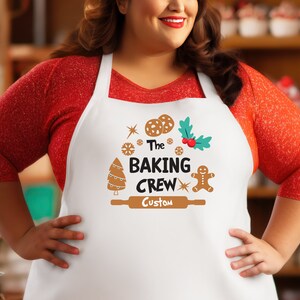 Puede incluir: Delantal blanco con un hombre de jengibre marr&oacute;n, un &aacute;rbol de Navidad y un rodillo. El texto en el delantal dice "The Baking Crew Custom".
