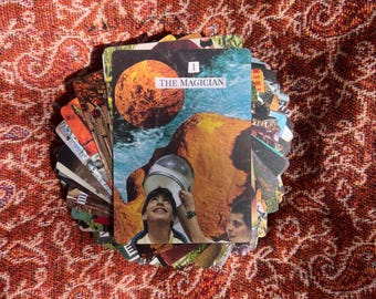 Puede incluir: Una baraja de cartas de tarot rectangulares en abanico, con la carta superior titulada The Magician. La carta presenta una ilustración de collage de una persona mirando hacia una cúpula de cristal, un gran planeta naranja y rocas.