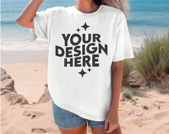 May include: A white t-shirt with the text "YOUR DESIGN HERE" in black lettering and a star design. The shirt is being worn by a person on a beach.