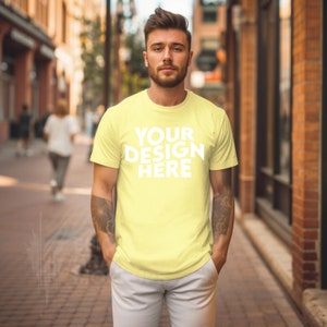 Könnte beinhalten: Ein Mann trägt ein gelbes T-Shirt mit dem Aufdruck "YOUR DESIGN HERE" auf der Vorderseite. Er steht in einer Stadtstraße.