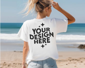 May include: White t-shirt with the text "YOUR DESIGN HERE" printed on the back. The shirt is being worn by a person on a beach.