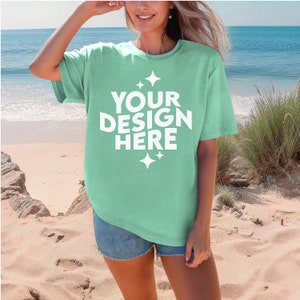May include: A light green t-shirt with short sleeves and a crew neck. The shirt has the text "YOUR DESIGN HERE" printed on the front in white with small white stars.