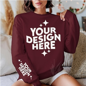 May include: A maroon sweatshirt with white text that says "YOUR DESIGN HERE" on the front and "YOUR DESIGN HERE" on the sleeve. The sweatshirt has a crew neck and long sleeves.