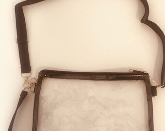 May include: Clear plastic crossbody bag with a black adjustable strap. The bag has a zipper closure and a clear interior.