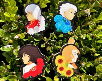 Pode incluir: Quatro pinos de madeira com personagens e detalhes florais. Os pinos mostram um personagem de cabelo branco com flores vermelhas, um personagem loiro com girassóis, um personagem de cabelo castanho com flores vermelhas e um personagem de cabelo branco com flores azuis.