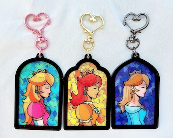 May include: Three stained glass style keychains featuring different princesses. Each keychain has a heart-shaped metal ring and a black border. The princesses are depicted in a stained glass style with colorful backgrounds.