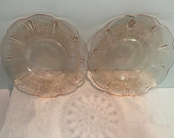 May include: Two pink glass dessert plates with a floral pattern. The plates have a scalloped edge.
