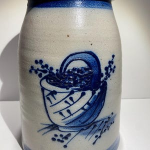 May include: A blue and white stoneware crock with a blue and white painted design of a basket filled with berries. The crock has a wide mouth and a rounded body.