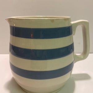 May include: A white ceramic jug with blue stripes. The jug has a handle and a rounded body.
