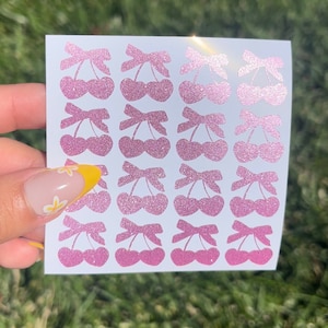 Puede incluir: Una hoja de pegatinas de cerezas con purpurina rosa con un lazo en la parte superior. Hay 20 pegatinas en la hoja.