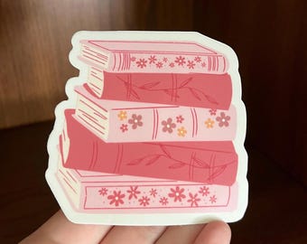May include: A stack of four pink books with floral and leaf designs. The books are stacked on top of each other and have a white background.