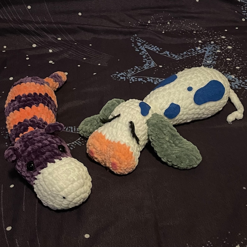 May include: Two crocheted stuffed animals, one a purple and orange striped worm and the other a white, blue, and green dog with a pink nose.