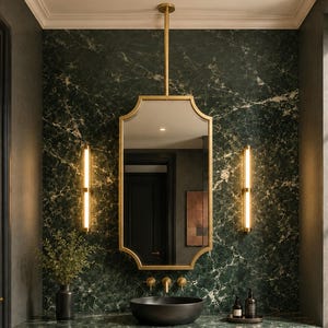 Puede incluir: Un mueble de baño con encimera y salpicadero de mármol verde oscuro, un lavabo negro, un espejo con marco dorado suspendido del techo y dos apliques de pared dorados verticales que proporcionan una iluminación cálida.