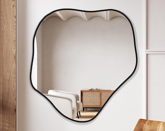 Puede incluir: Un sillón de cuero marrón con una lámpara de pie de metal negro en una habitación con un gran espejo negro de forma irregular en la pared.