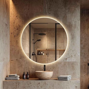 Puede incluir: Un baño moderno con un espejo redondo iluminado, una encimera de piedra con un lavabo y un inodoro negro. Las paredes están hechas de piedra texturizada.