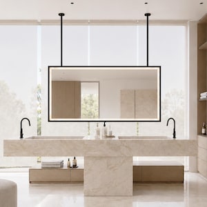 May include: A rectangular wall-mounted mirror with a black frame and integrated LED lighting, suspended from the ceiling by two black rods above a double vanity made of beige marble with two black faucets and integrated sinks.